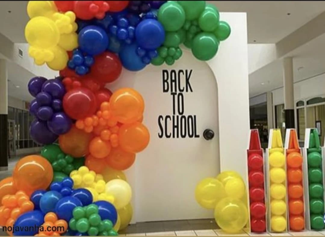 دکوراسیون بازگشت به مدرسه با طاق بادکنکی رنگینکمانی دور در سفید نوشته BACK TO SCHOOL و چهار استند مداد رنگی بادکنکی قرمز زرد نارنجی و سبز